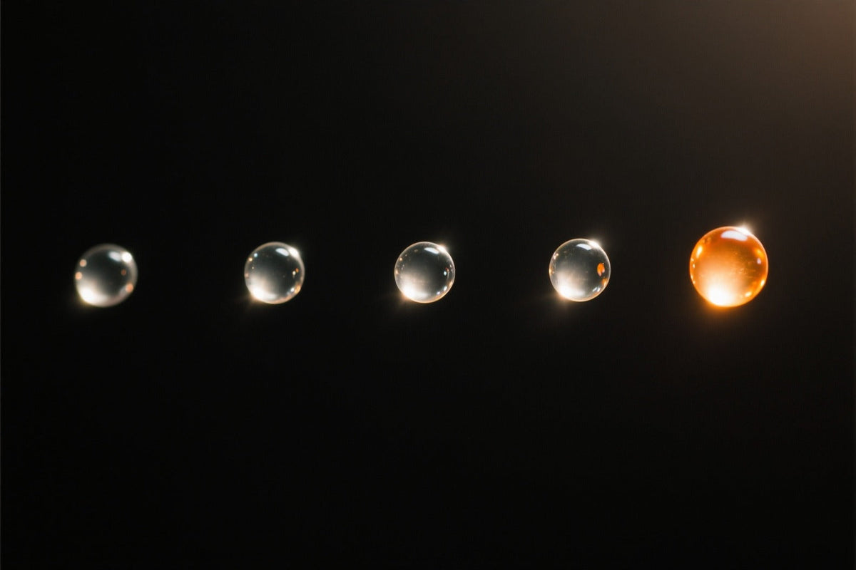 Five clear gel beads in a row floating on a dark background, the one at the right end glowing warm orange