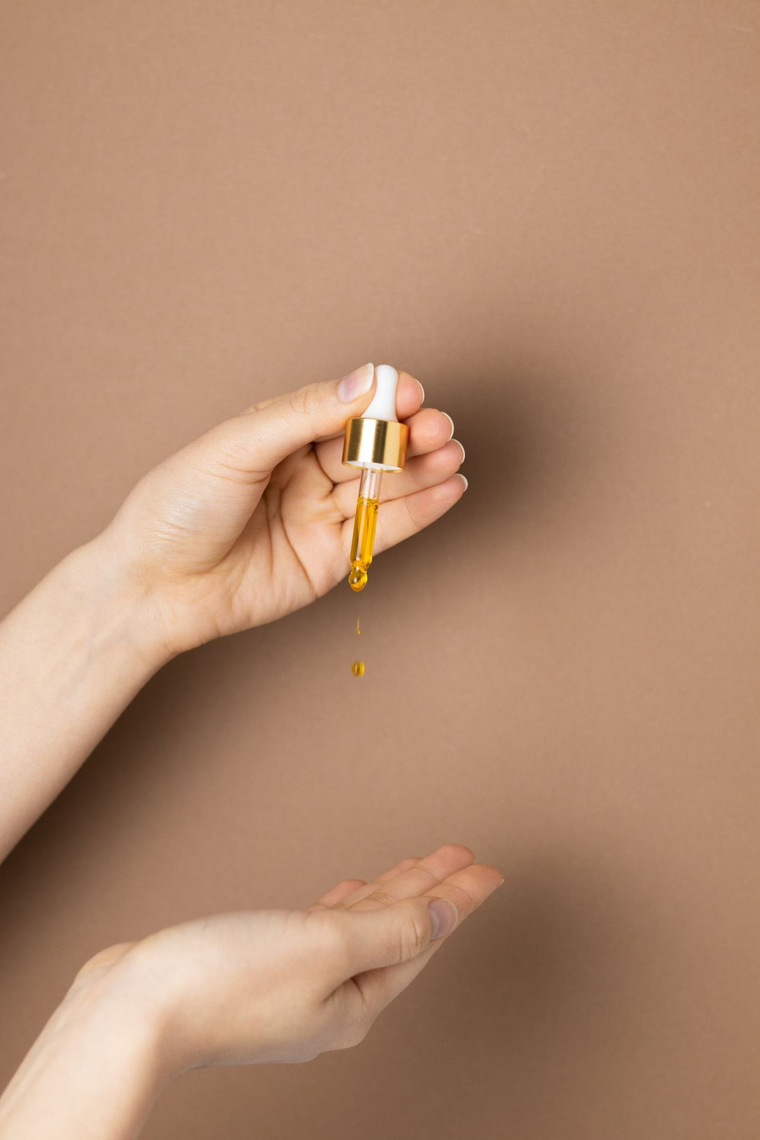 Golden facial oil dispensed from a dropper onto skin