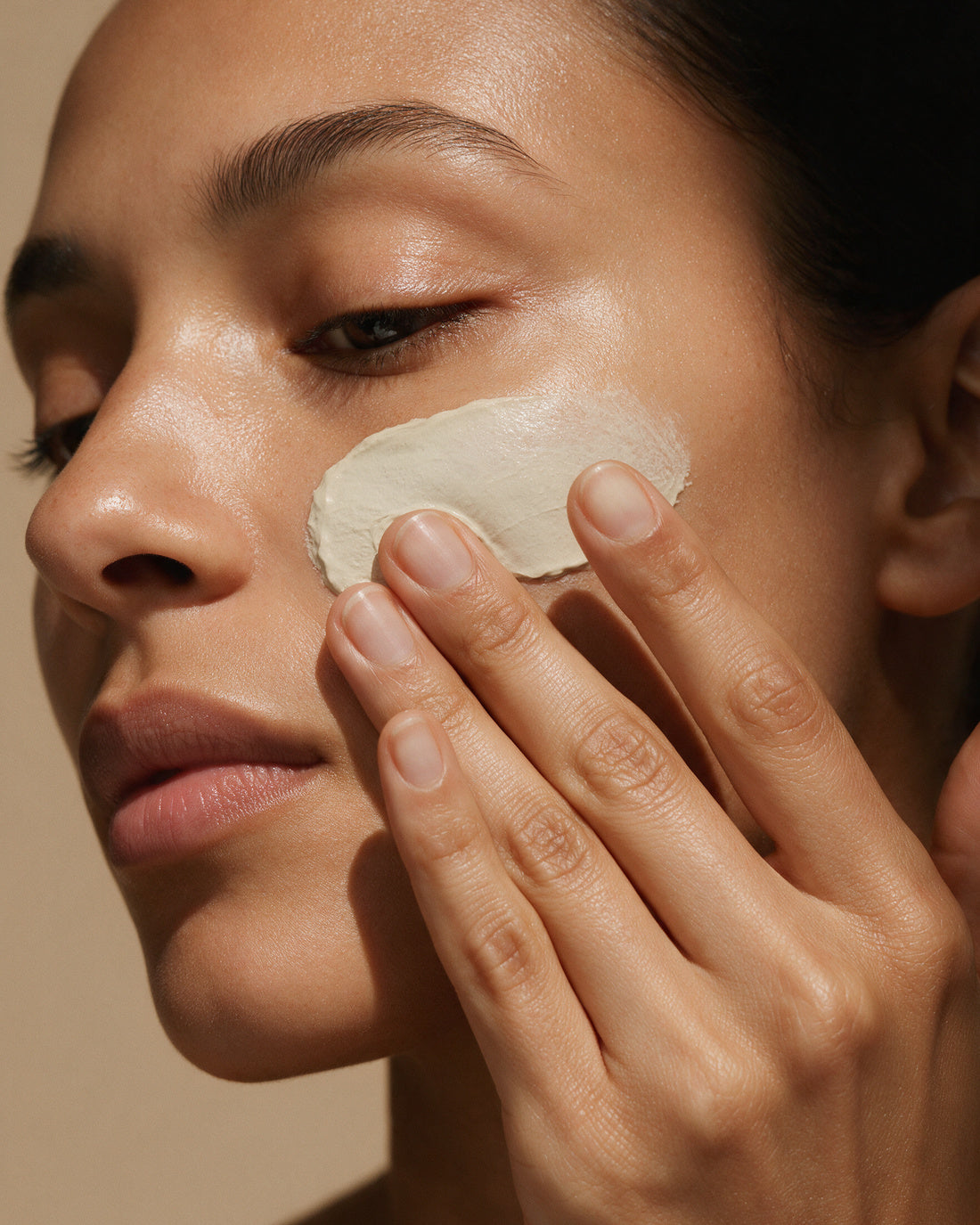 A smooth pale clay mask being smoothed across the cheekbone