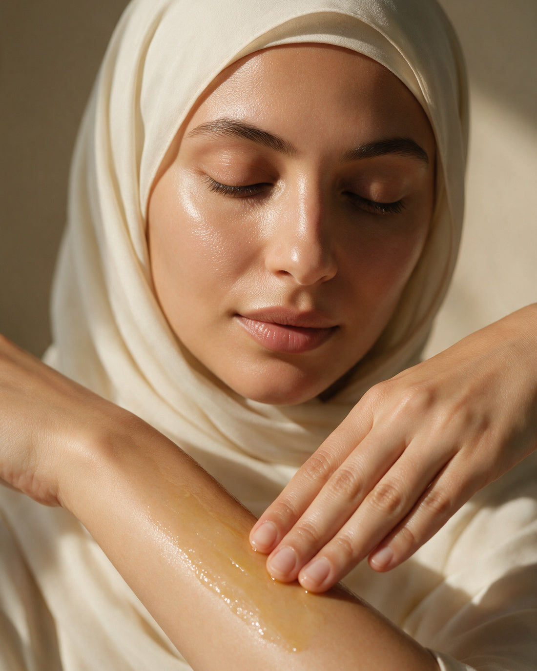 A hand smoothing a thin veil of golden oil along a bare forearm, soft glow