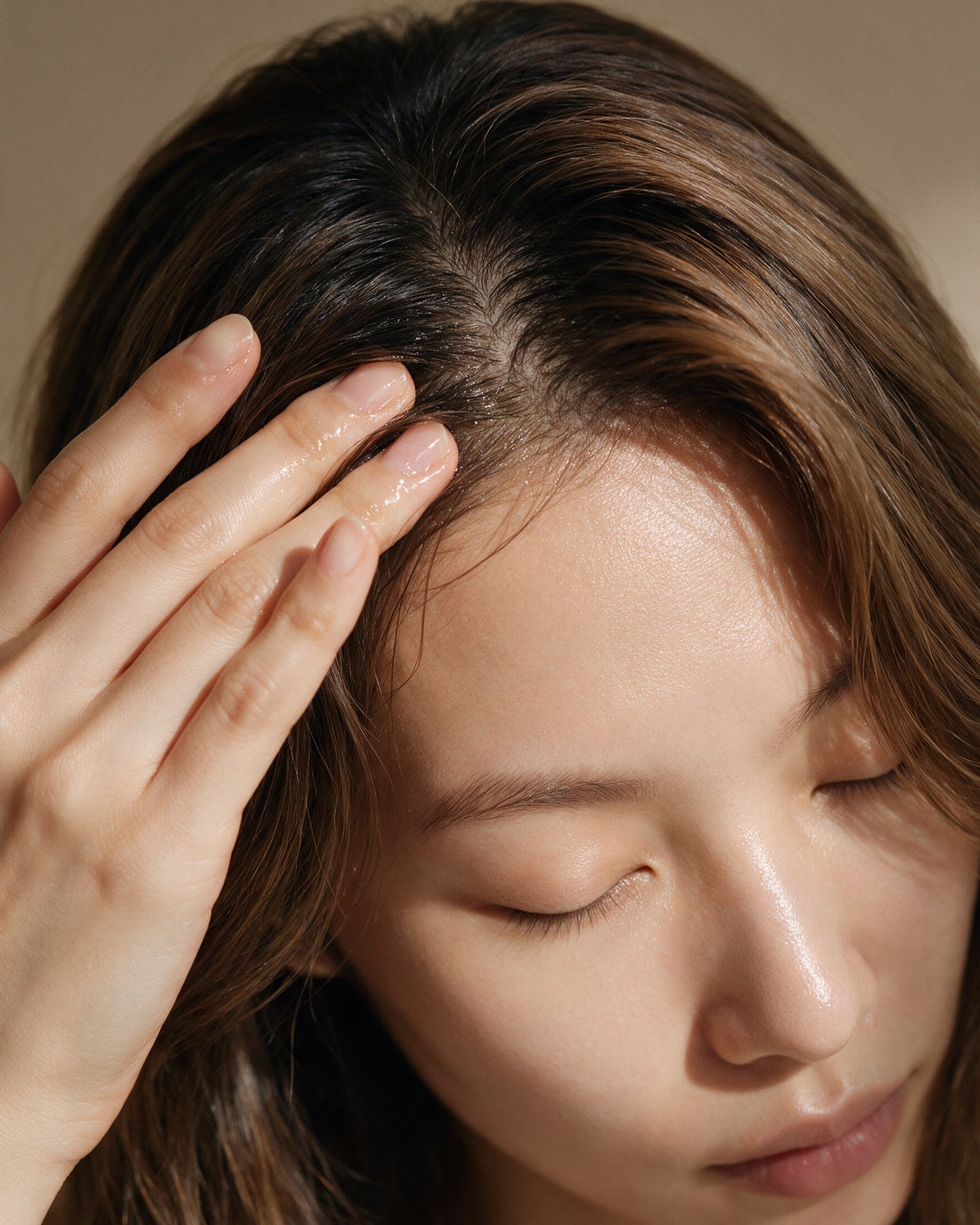 Fingertips parting the hair at the scalp with a light serum sheen