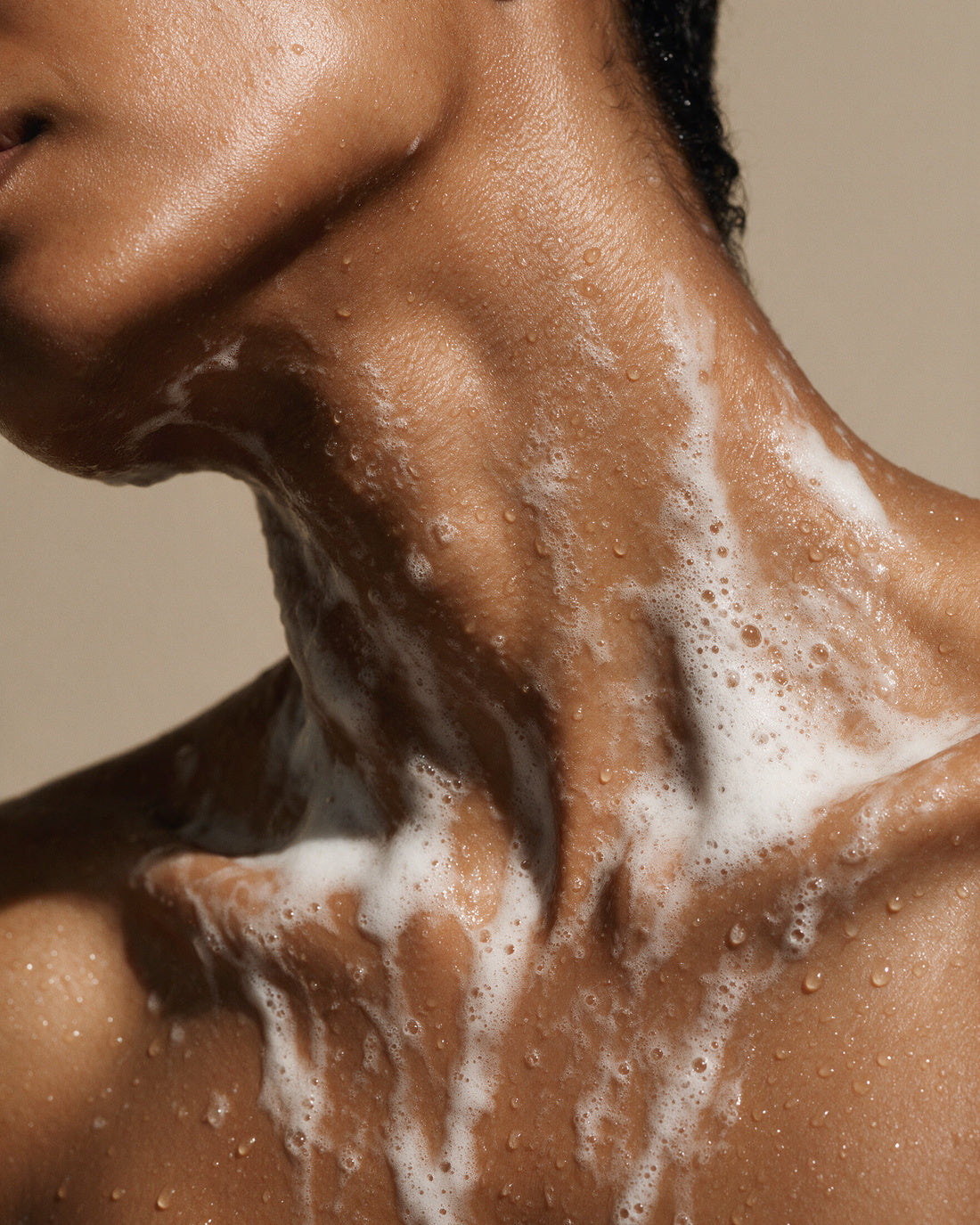 PEPPERMINT CEDAR BODY WASH rinsing as white lather from the neck and collarbone, head turned away.