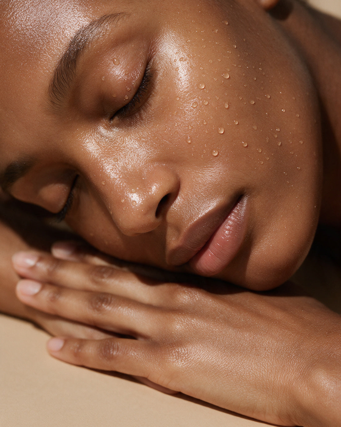 Fine water mist settling on a luminous cheek and closed eye, droplets catching light