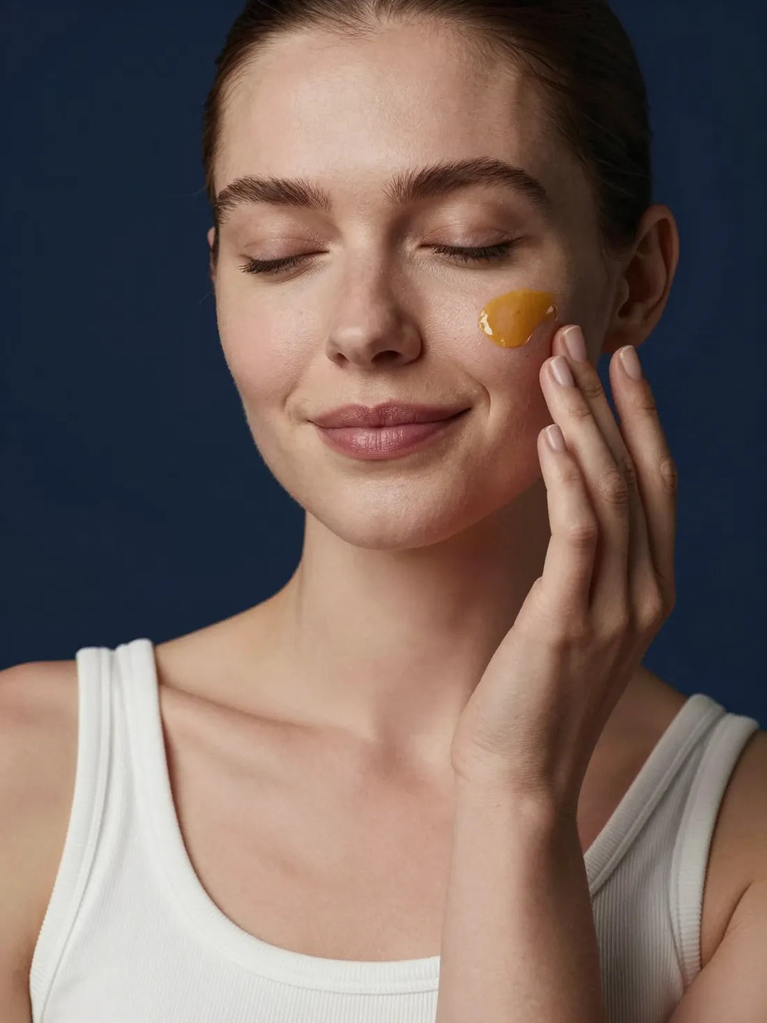 A golden facial oil pressed into the cheek with the fingertips, eyes closed, CELLULAR ANTI-AGING BAKUCHIOL RENEWAL OIL