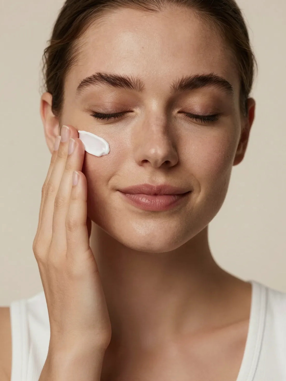 A white cream pressed into the cheekbone with the fingertips, eyes closed, HEXAPEPTIDE FIRMING SERUM