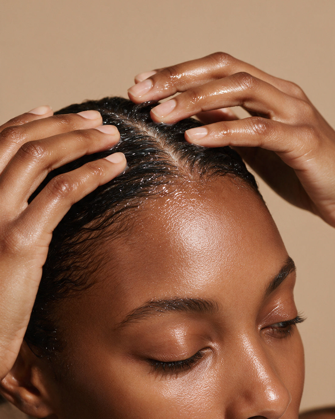 Fingertips parting the hair at the scalp with a light serum sheen