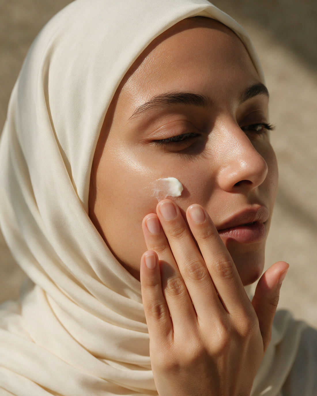 Fingertips pressing a small dab of rich white cream into the cheek