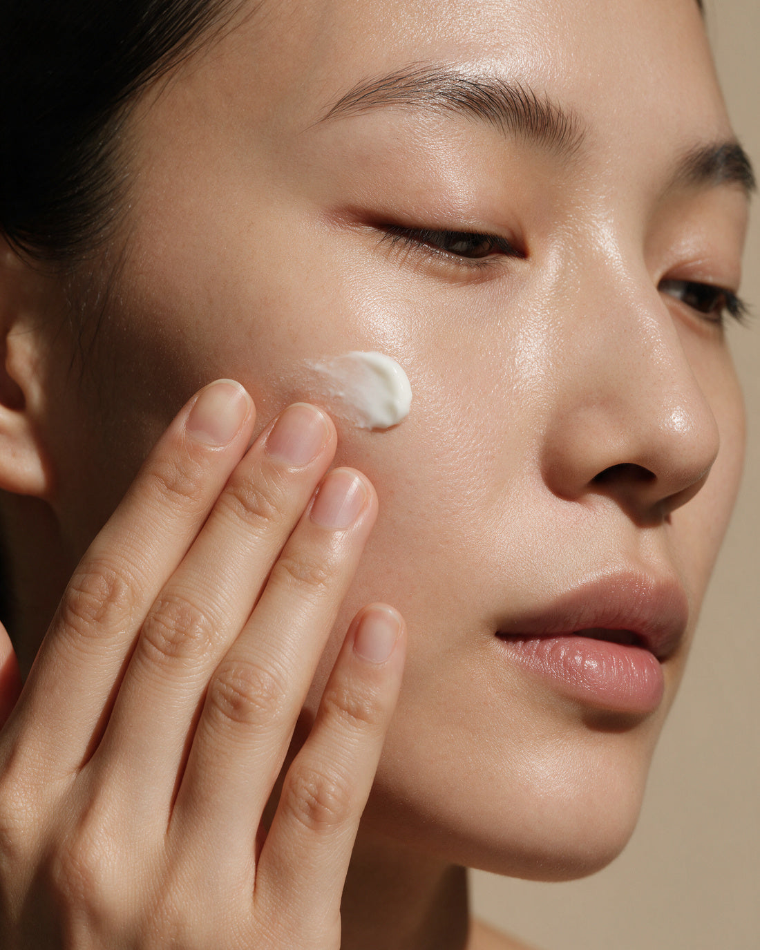 Fingertips pressing a small dab of rich white cream into the cheek