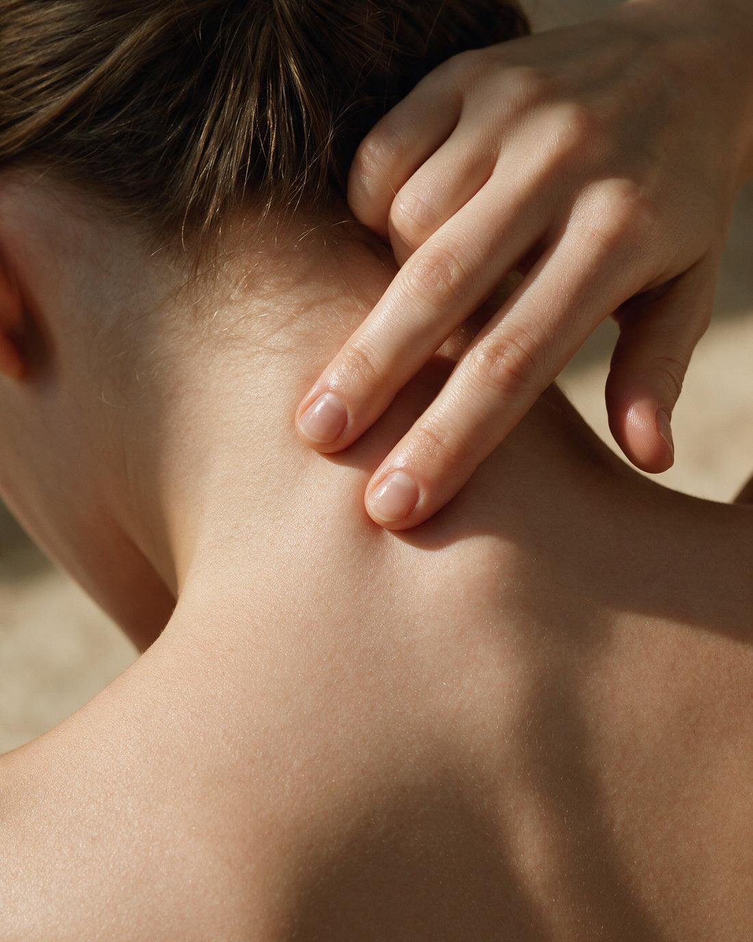 Editorial frame for the HYDRATING BODY SERUM SANDALWOOD: two fingers drawn down the nape of the neck, head bowed forward.