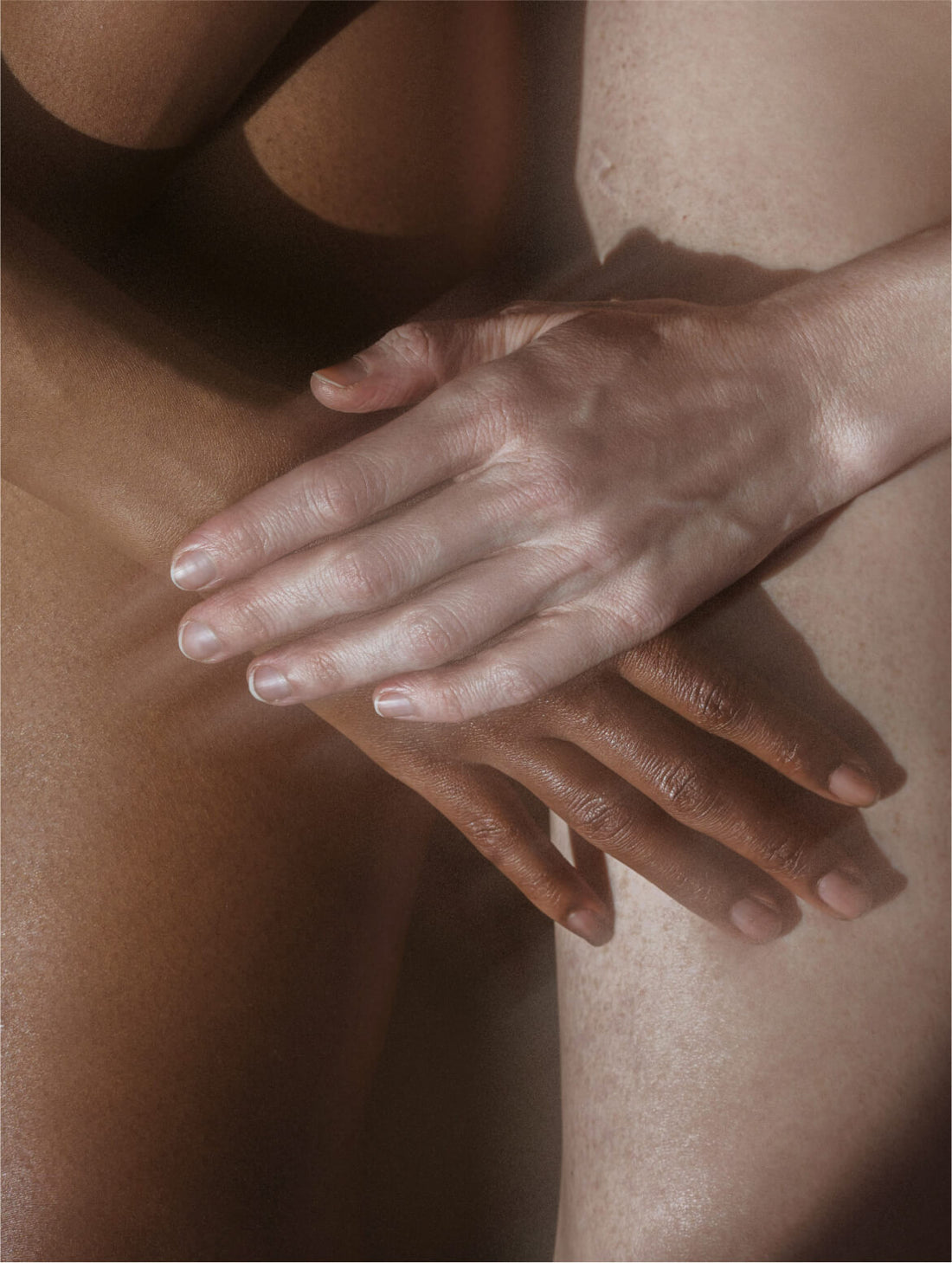 A hand resting across another against bare skin, two skin tones, UREA RENEWAL BODY CREAM
